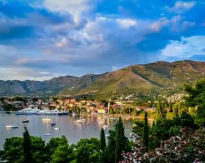 Cavtat boats on body of water surrounded by trees and houses near mountain under blue and white sky at daytime