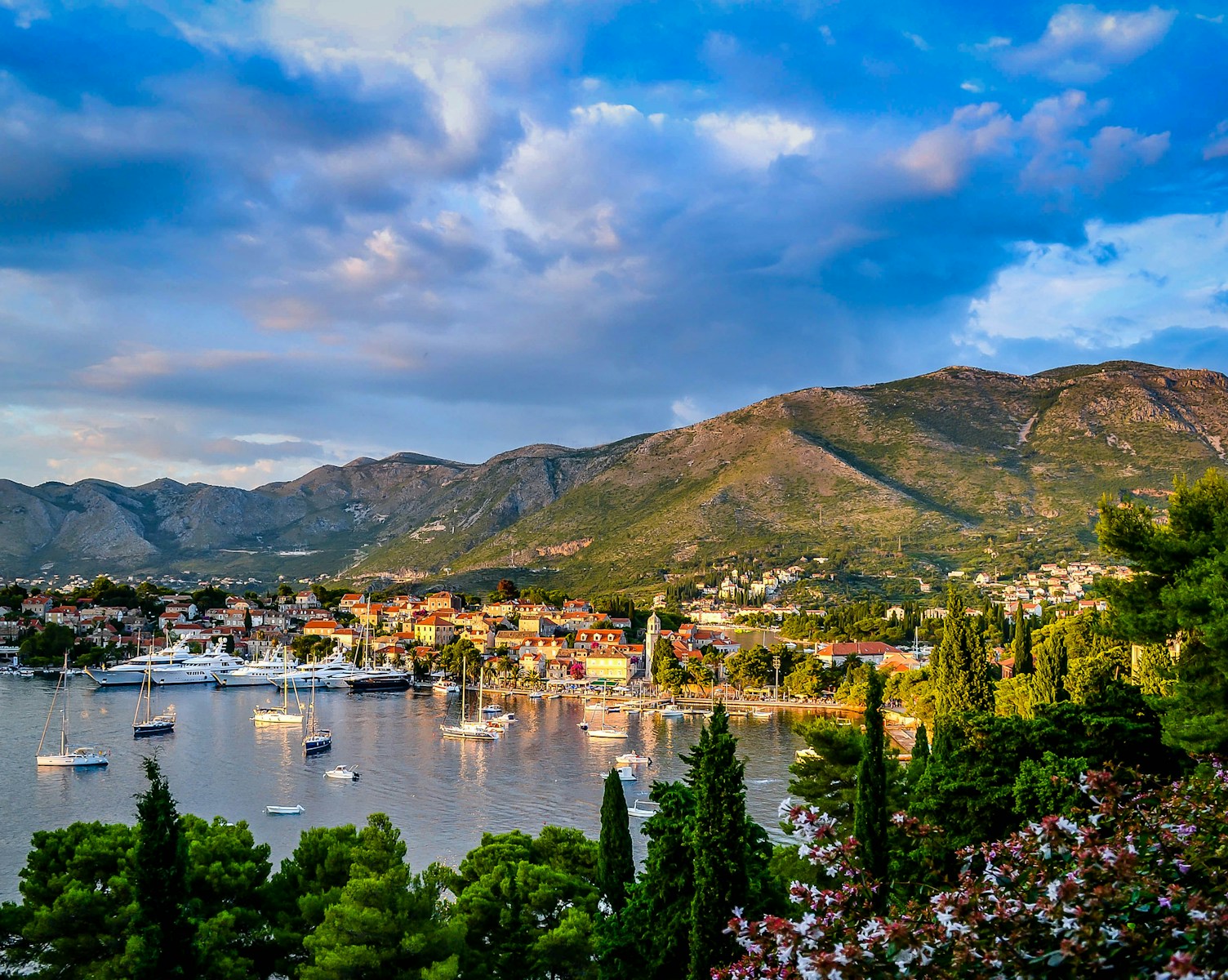 Cavtat boats on body of water surrounded by trees and houses near mountain under blue and white sky at daytime